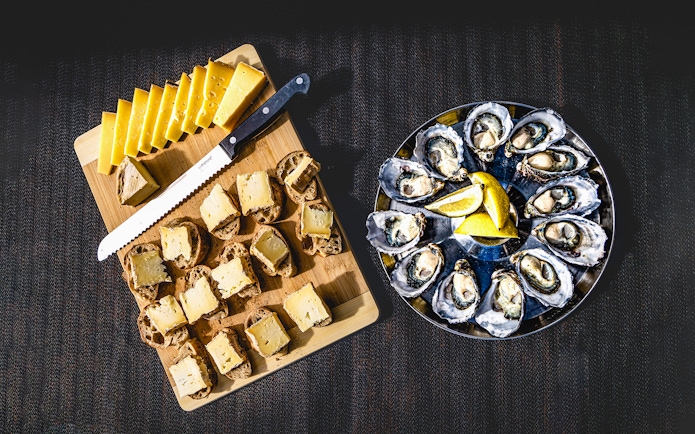 Bread with cheese and oysters served with lemon slices on a platter.