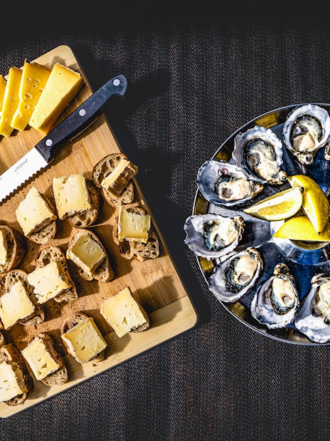 Bread with cheese and oysters served with lemon slices on a platter.