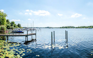 Boats docked on Havel River near Heiligensee, Berlin, with lily pads and clear sky.