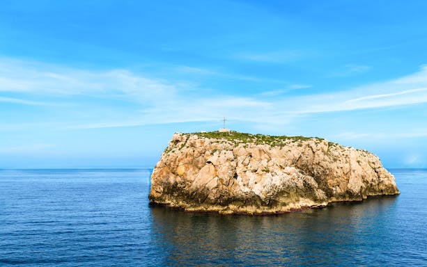 Rocky island with a cross in the sea near Polignano a Mare, Italy.