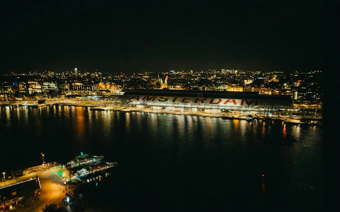Aerial view of Amsterdam Central Station and city lights reflecting on the canal at night.