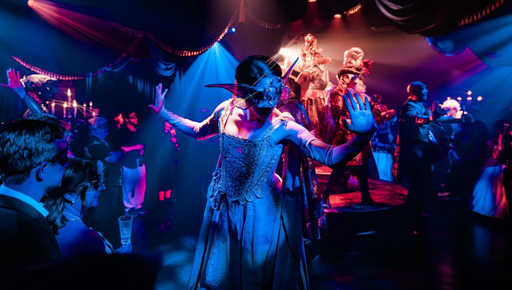 Masquerade ball scene from Broadway performance with masked dancers on stage.