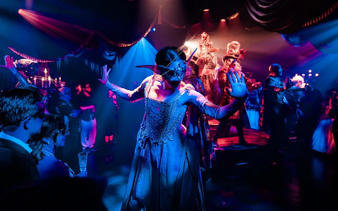 Masquerade ball scene from Broadway performance with masked dancers on stage.