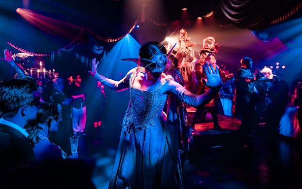 Masquerade ball scene from Broadway performance with masked dancers on stage.