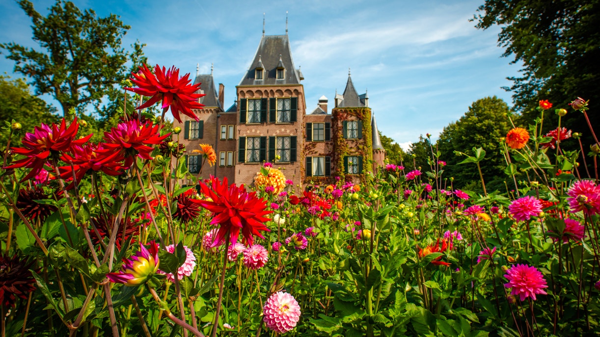 Dahlias in orange and red bloom in front of Keukenhof Castle on a sunny day.