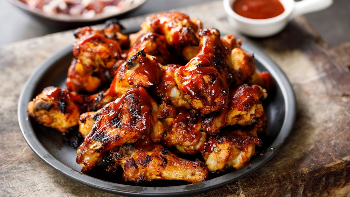 Barbecue chicken wings on a plate with dipping sauce in the background.