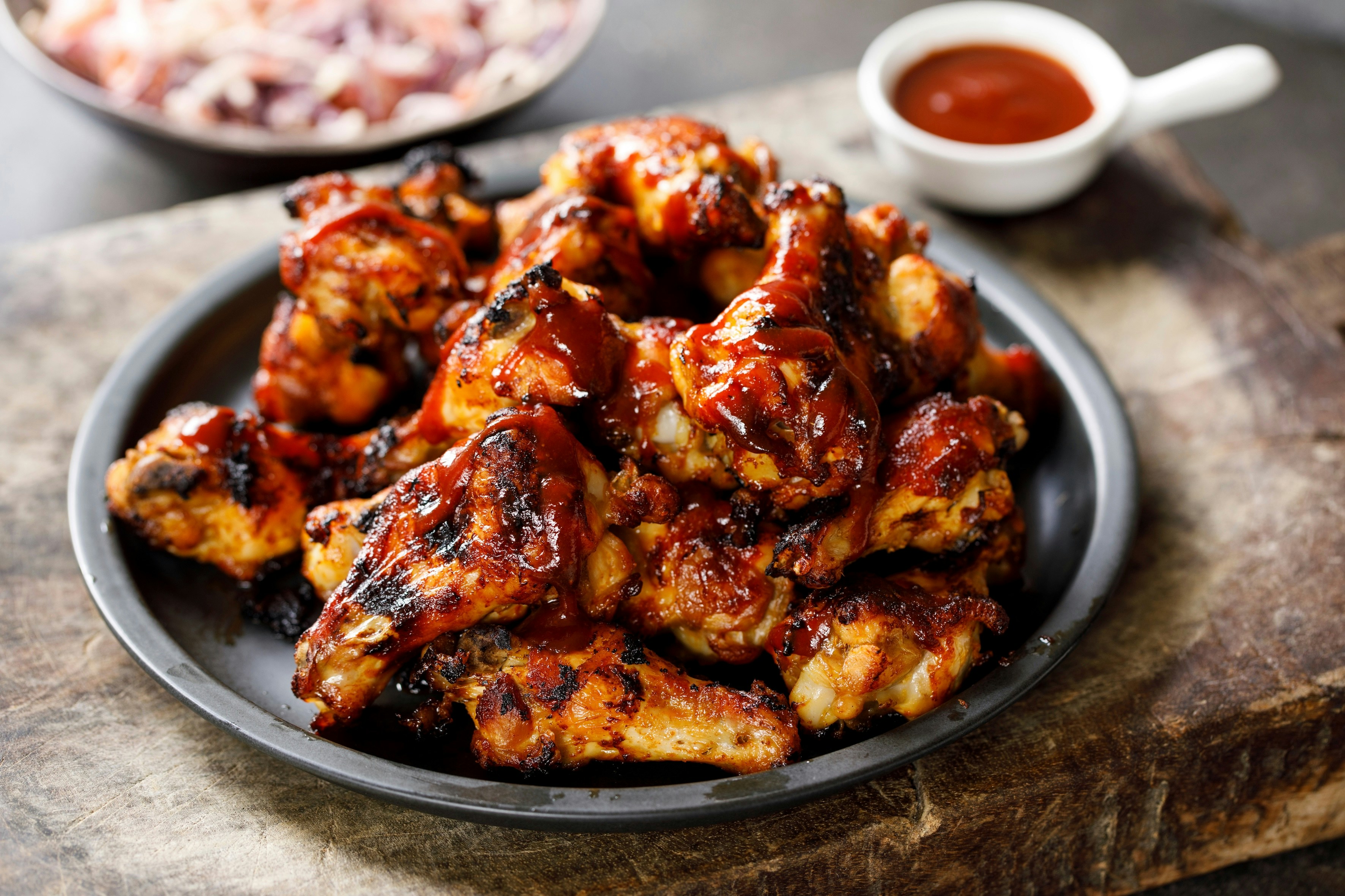 Barbecue chicken wings on a plate with dipping sauce in the background.