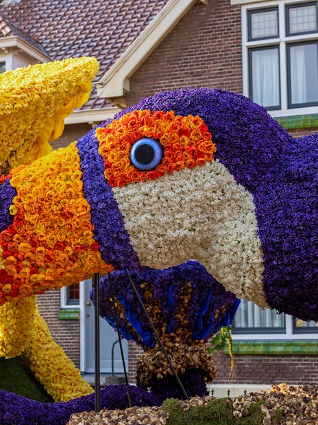 Toucan sculpture made of tulips and hyacinths in front of a brick building.