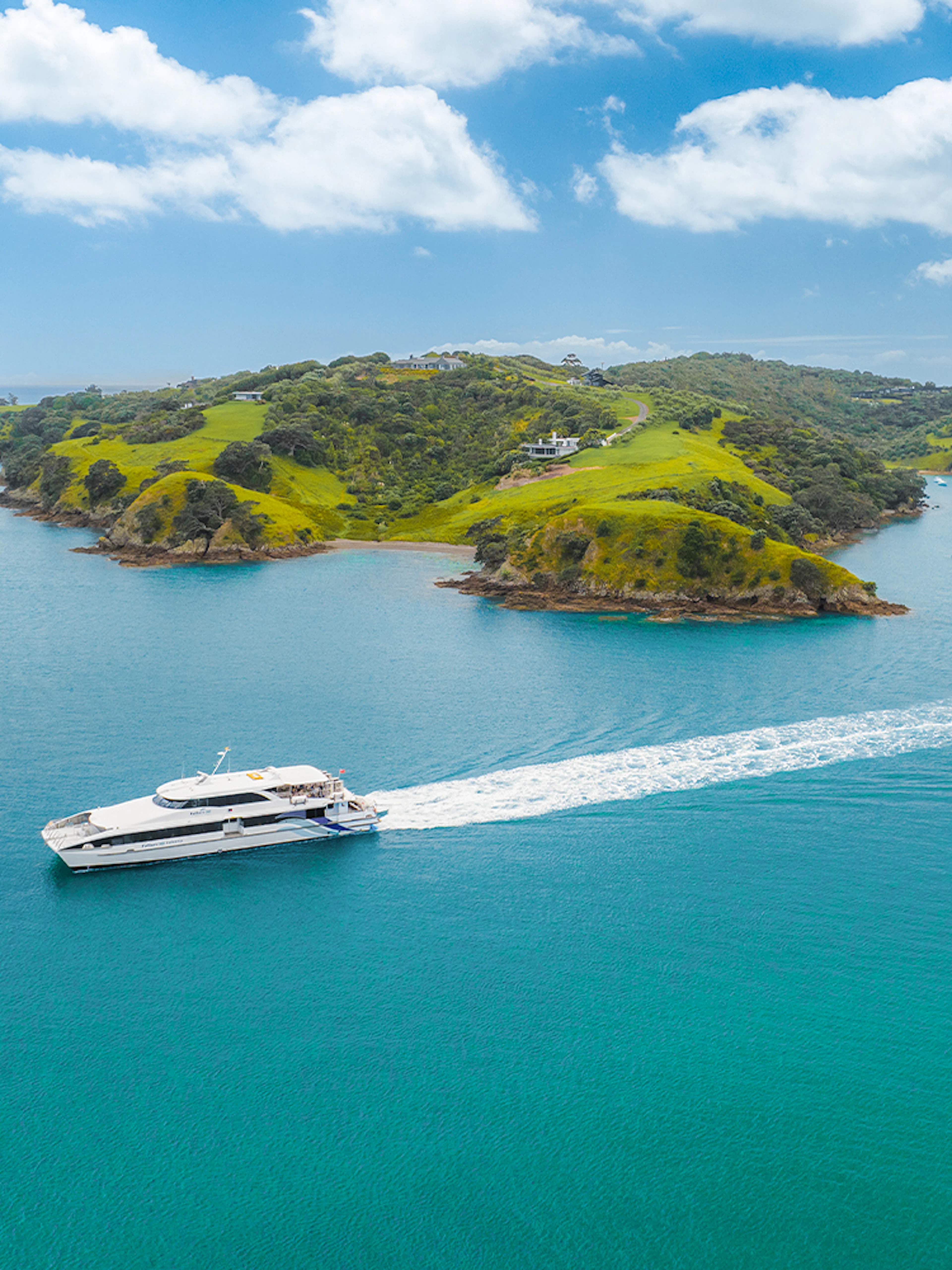 Ferry cruising near Waiheke Island with lush green hills and clear blue water.