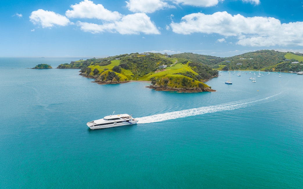 Ferry cruising near Waiheke Island with lush green hills and clear blue water.