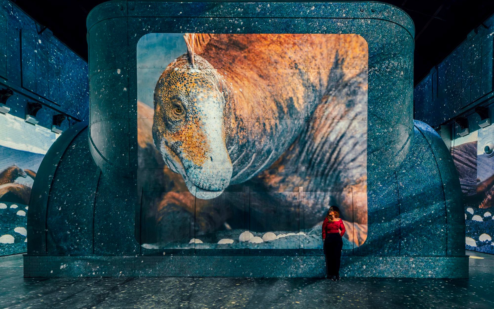 Dinosaur projection at Fabrique des Lumières exhibition with a visitor standing nearby.