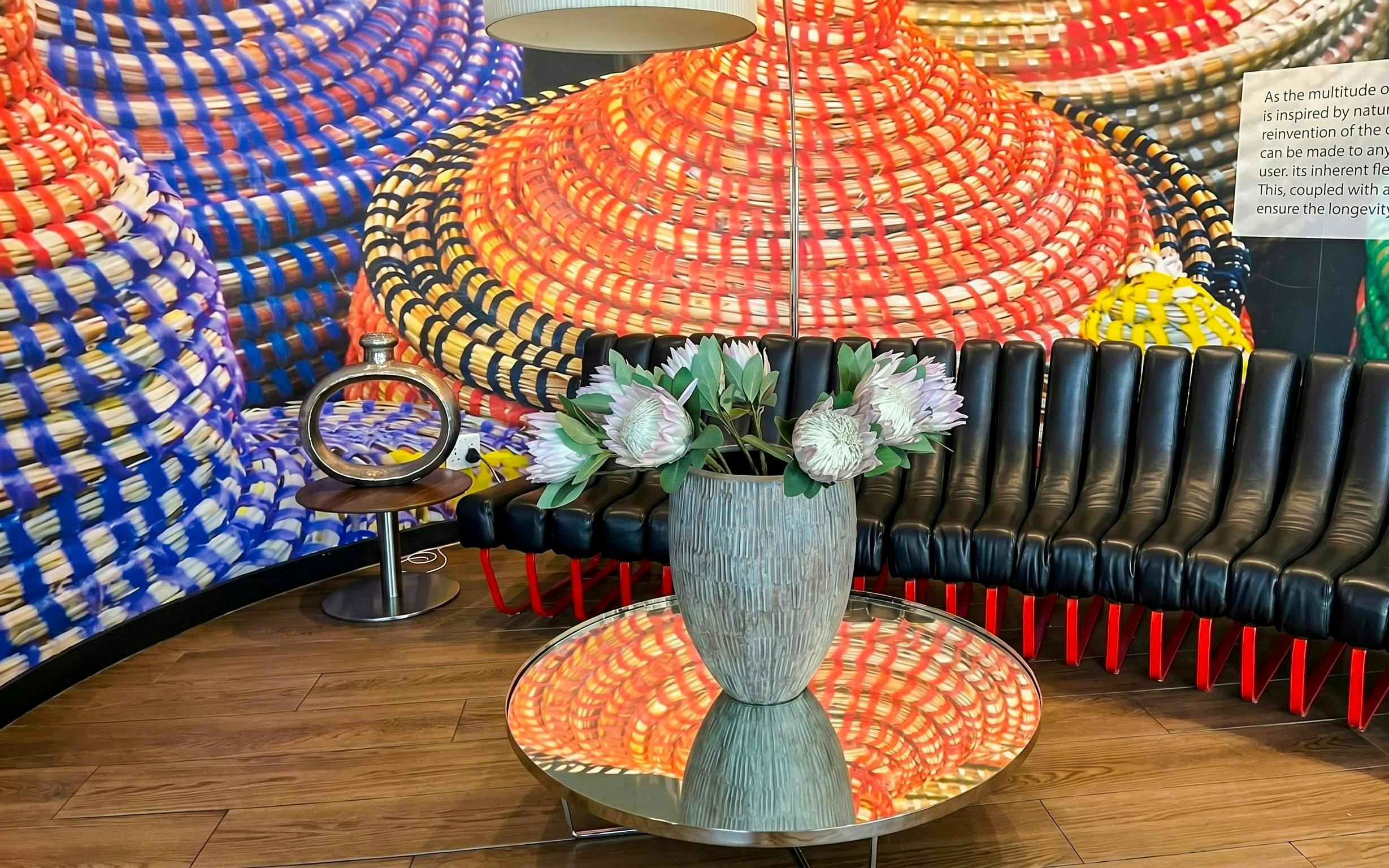 Shongololo Lounge seating area with protea flowers and colorful woven wall art at O. R. Tambo Airport Terminal A.