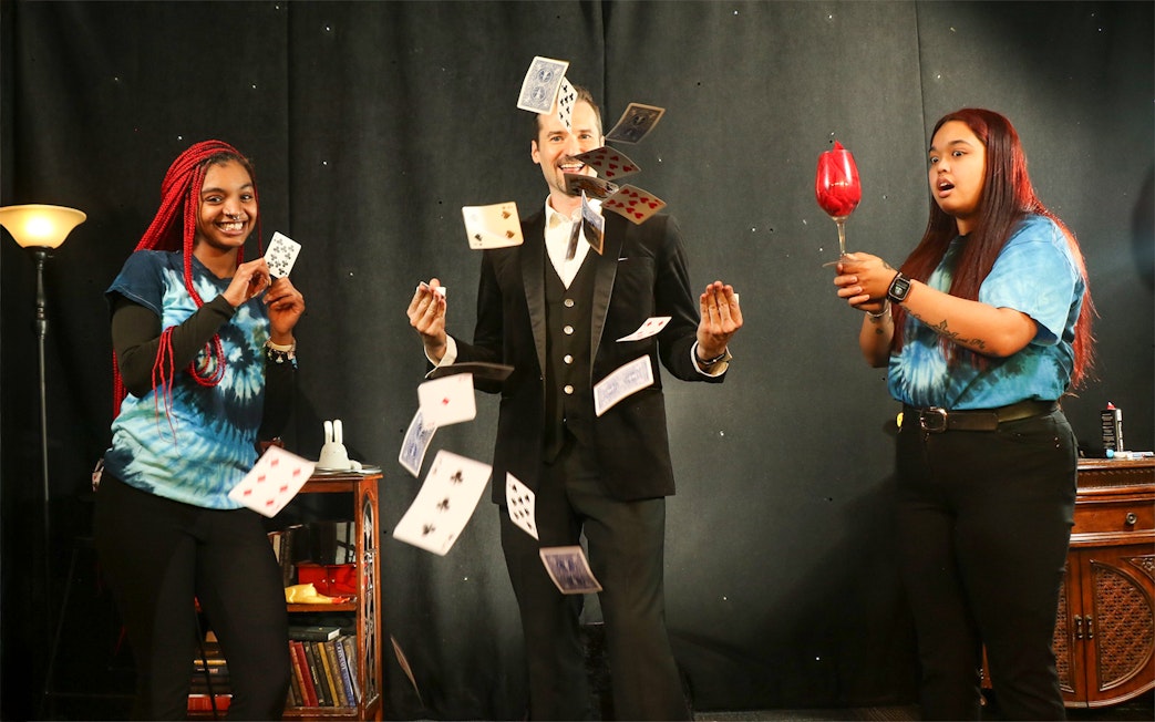 Magician performing card tricks with audience members on stage.