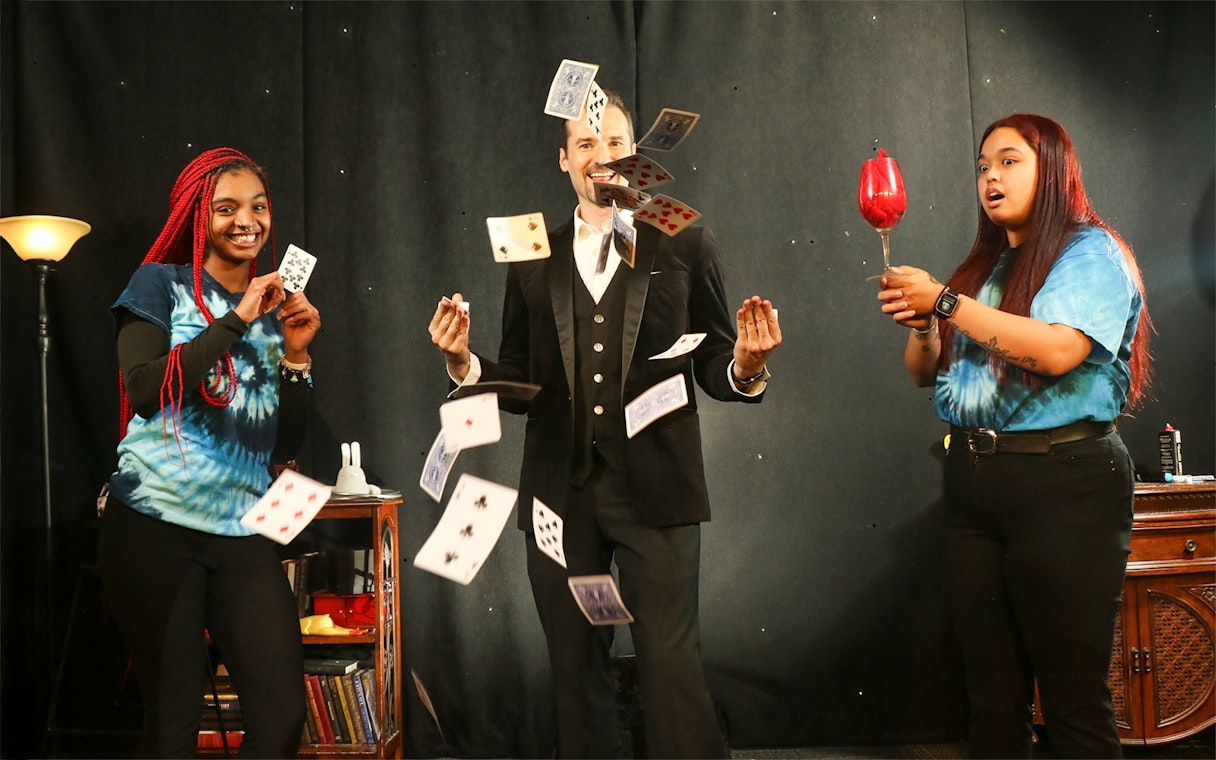Magician performing card tricks with audience members on stage.