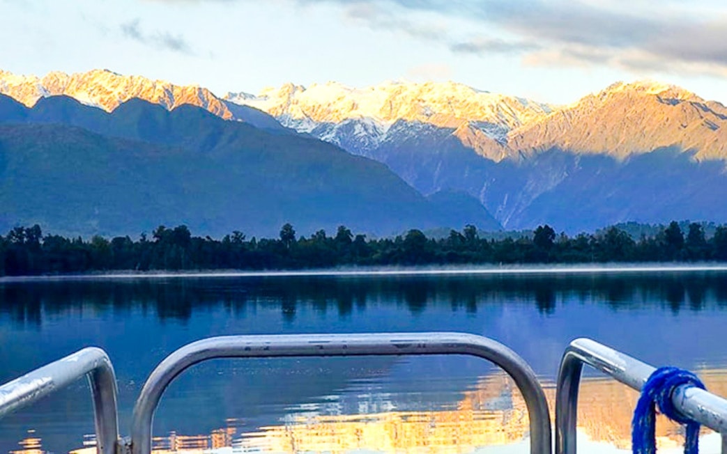 Boat view of Lake Mapourika with snow-capped mountains in the background.