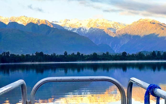 Boat view of Lake Mapourika with snow-capped mountains in the background.