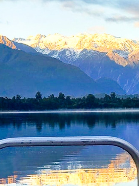 Boat view of Lake Mapourika with snow-capped mountains in the background.