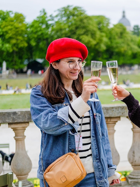 People clinking champagne glasses in a Paris park during Emily in Paris Food Tour.