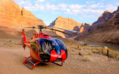 Helicopter on the Grand Canyon floor with canyon walls and river in the background.
