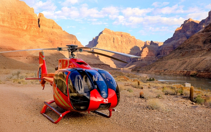Helicopter on the Grand Canyon floor with canyon walls and river in the background.