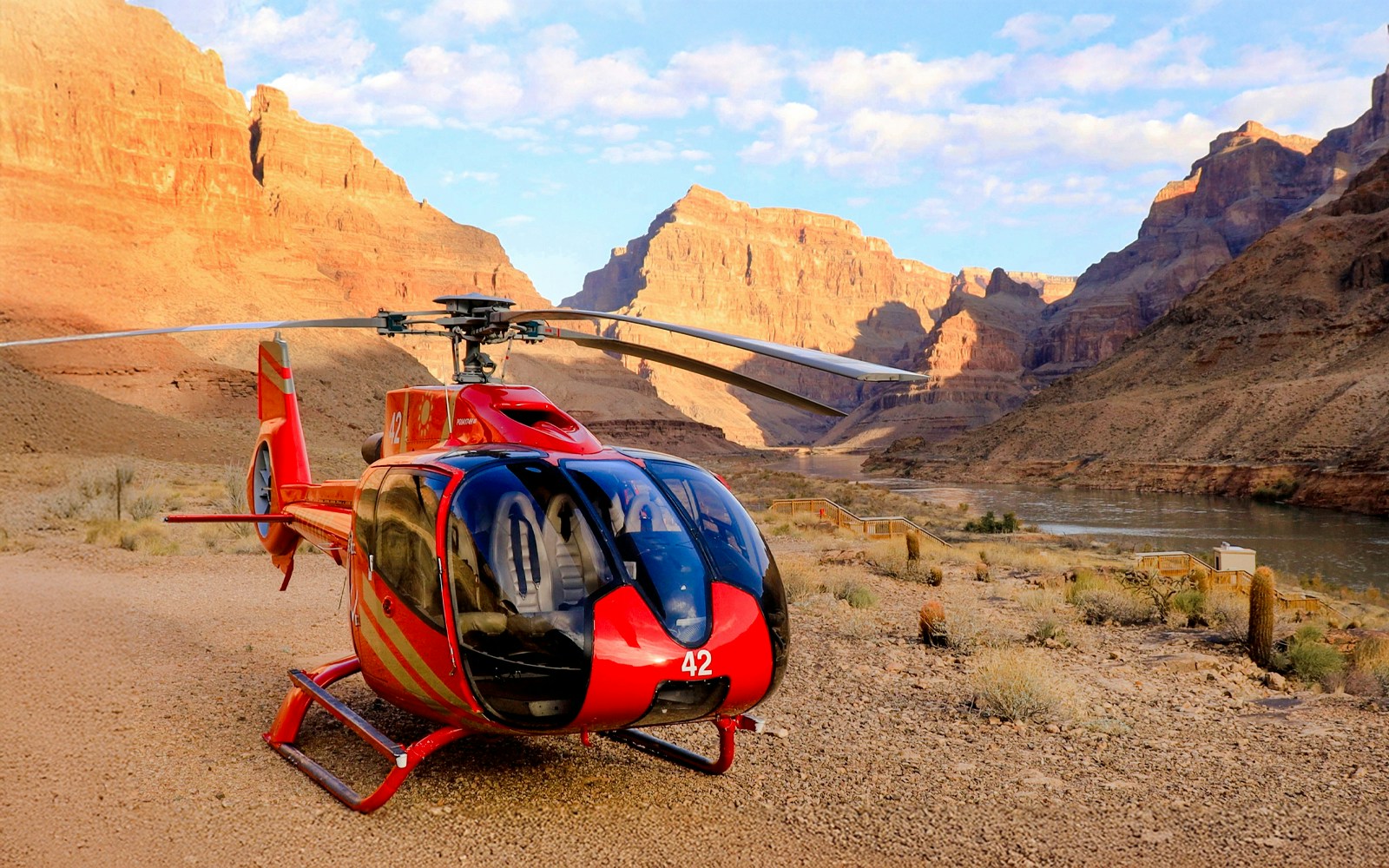 Helicopter on the Grand Canyon floor with canyon walls and river in the background.