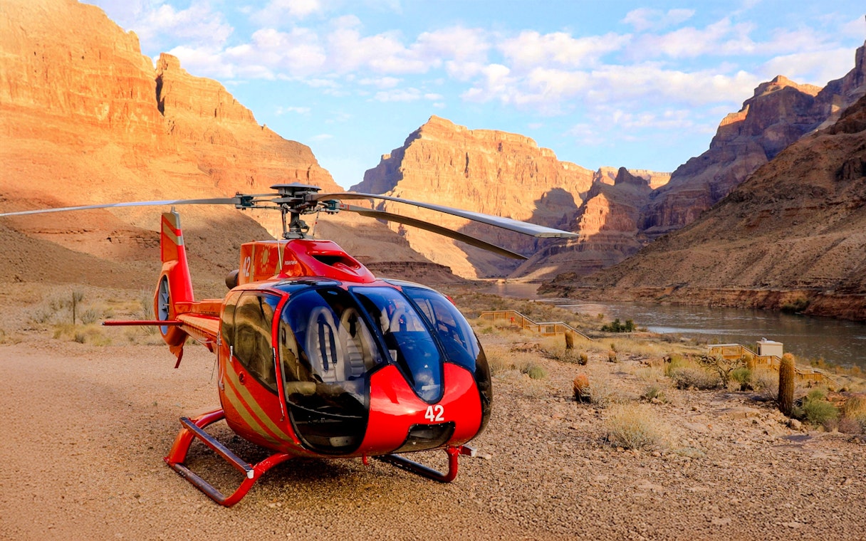Helicopter on the Grand Canyon floor with canyon walls and river in the background.
