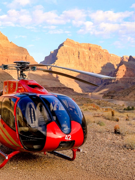 Helicopter on the Grand Canyon floor with canyon walls and river in the background.
