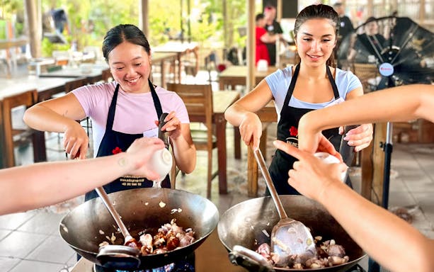 Participants cooking in a Nia Balinese cooking class, stirring ingredients in woks.
