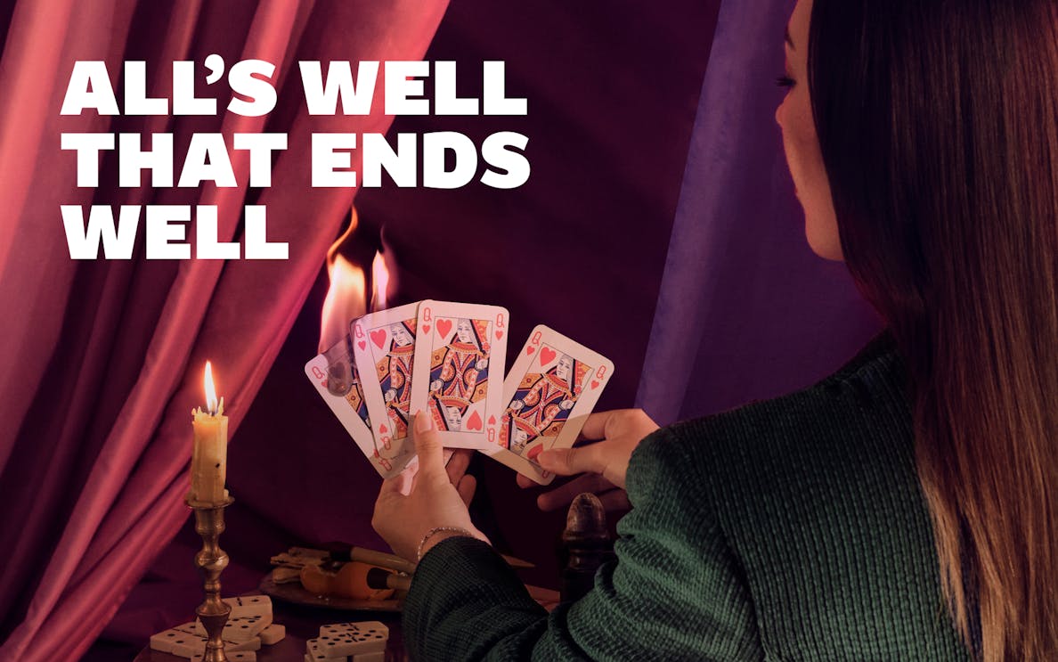 Person holding playing cards near candle with "All's Well that Ends Well" text.