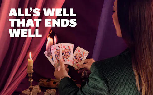 Person holding playing cards near candle with "All's Well that Ends Well" text.