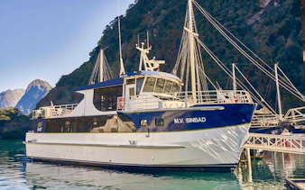Cruise boat docked at Milford Sound with scenic mountain backdrop.