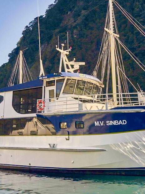 Cruise boat docked at Milford Sound with scenic mountain backdrop.