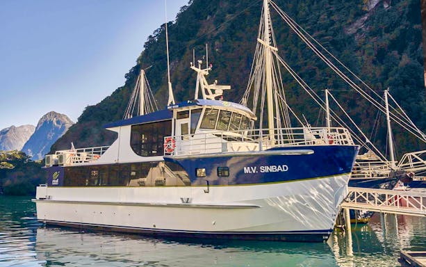 Cruise boat docked at Milford Sound with scenic mountain backdrop.