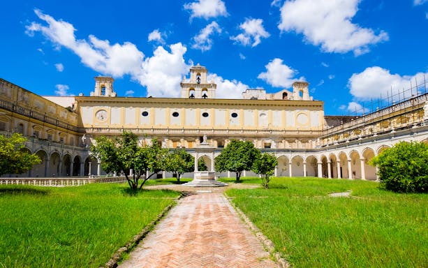 Courtyard of the Museum of San Martino with arches and greenery under a blue sky.