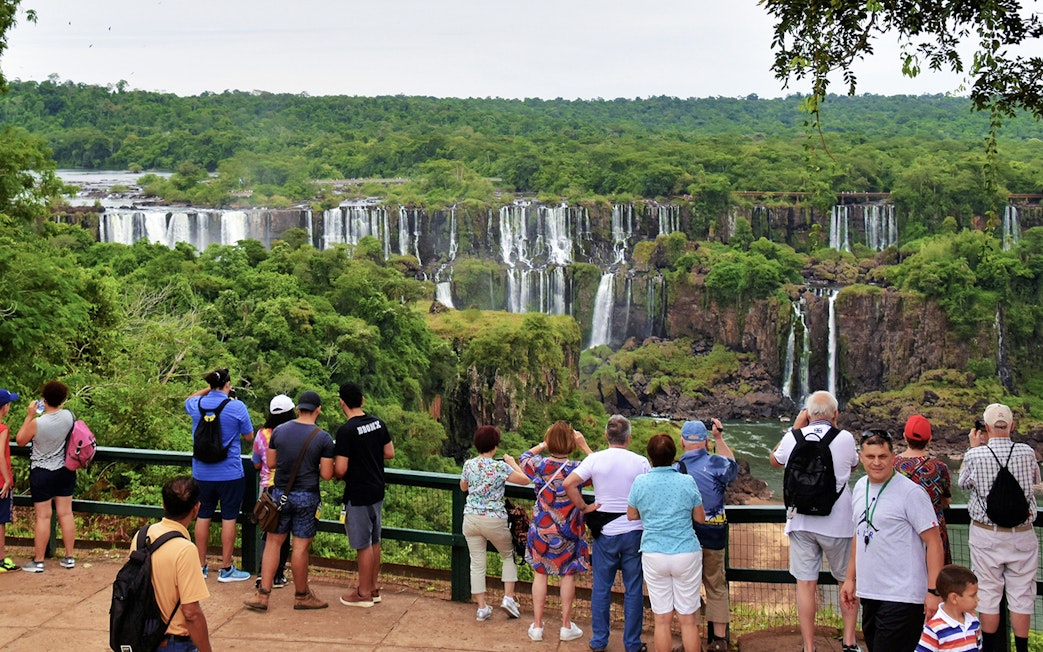 Visitors viewing Iguazu Falls from a lookout point surrounded by lush greenery.