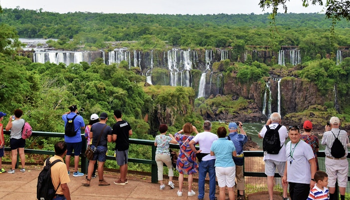 Visitors observing Iguazu Falls from the Argentine side, with lush greenery and cascading water.