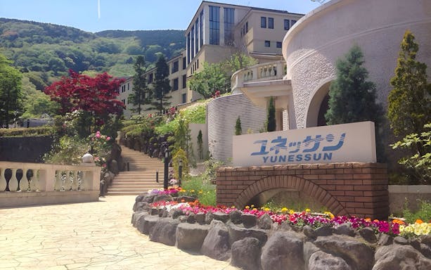 Hakone Kowakien Yunessun entrance with colorful flowers and mountain backdrop.