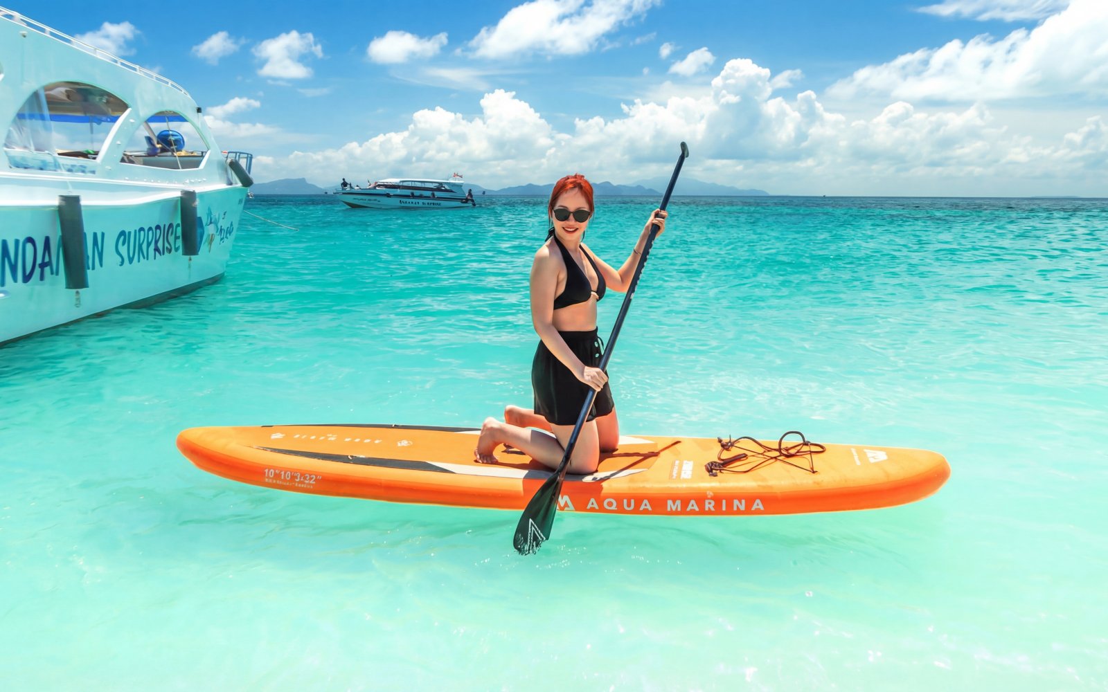 Person paddleboarding near speed catamaran in Phang Nga Bay, Thailand.