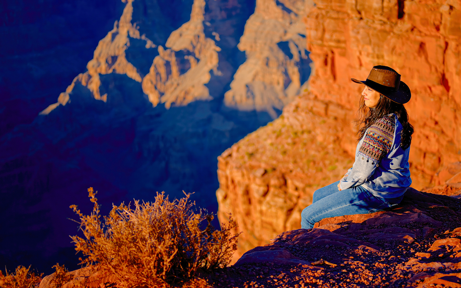 Cowgirl sitting on a rock ledge overlooking the Grand Canyon, Arizona.