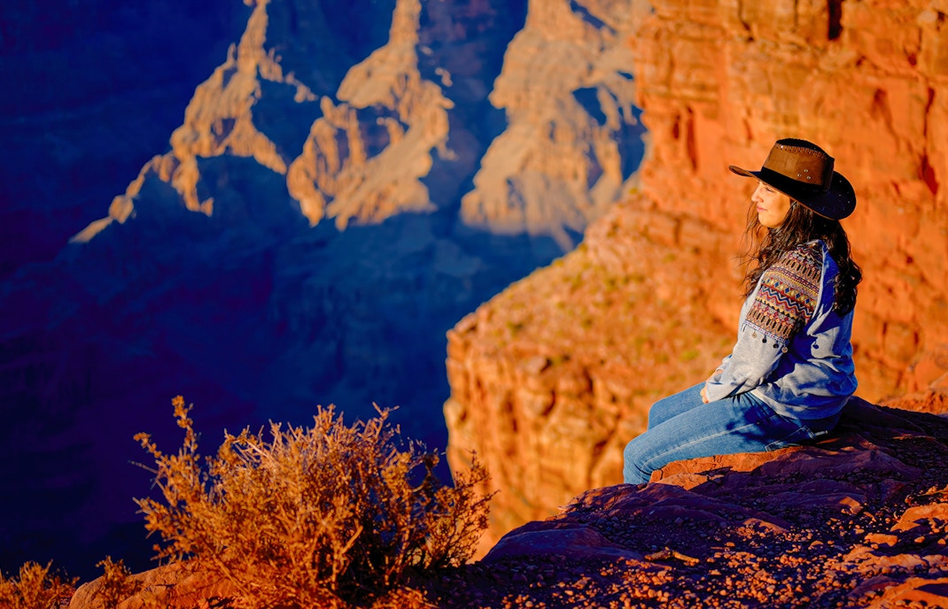Cowgirl sitting on a rock ledge overlooking the Grand Canyon, Arizona.
