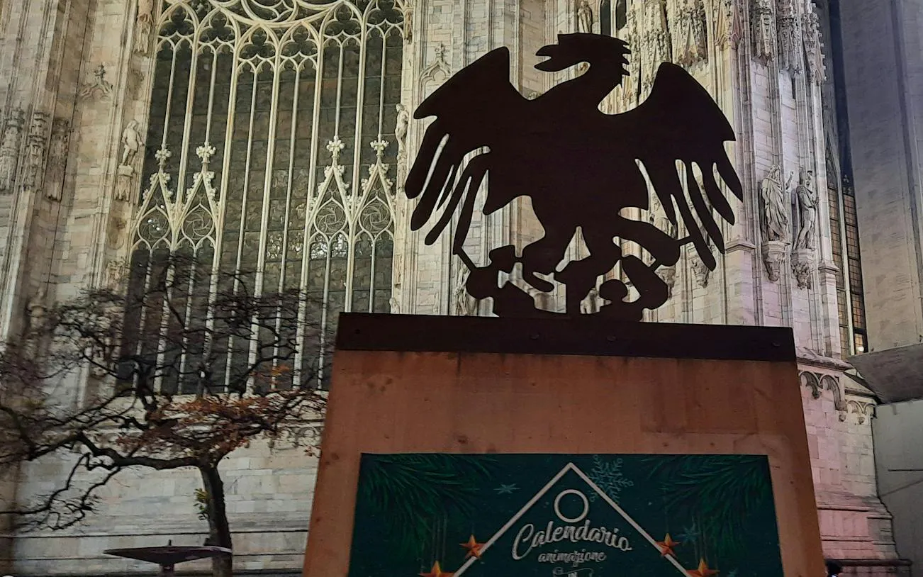 Silhouette of an eagle sculpture in front of Milan Cathedral during Christmas season.