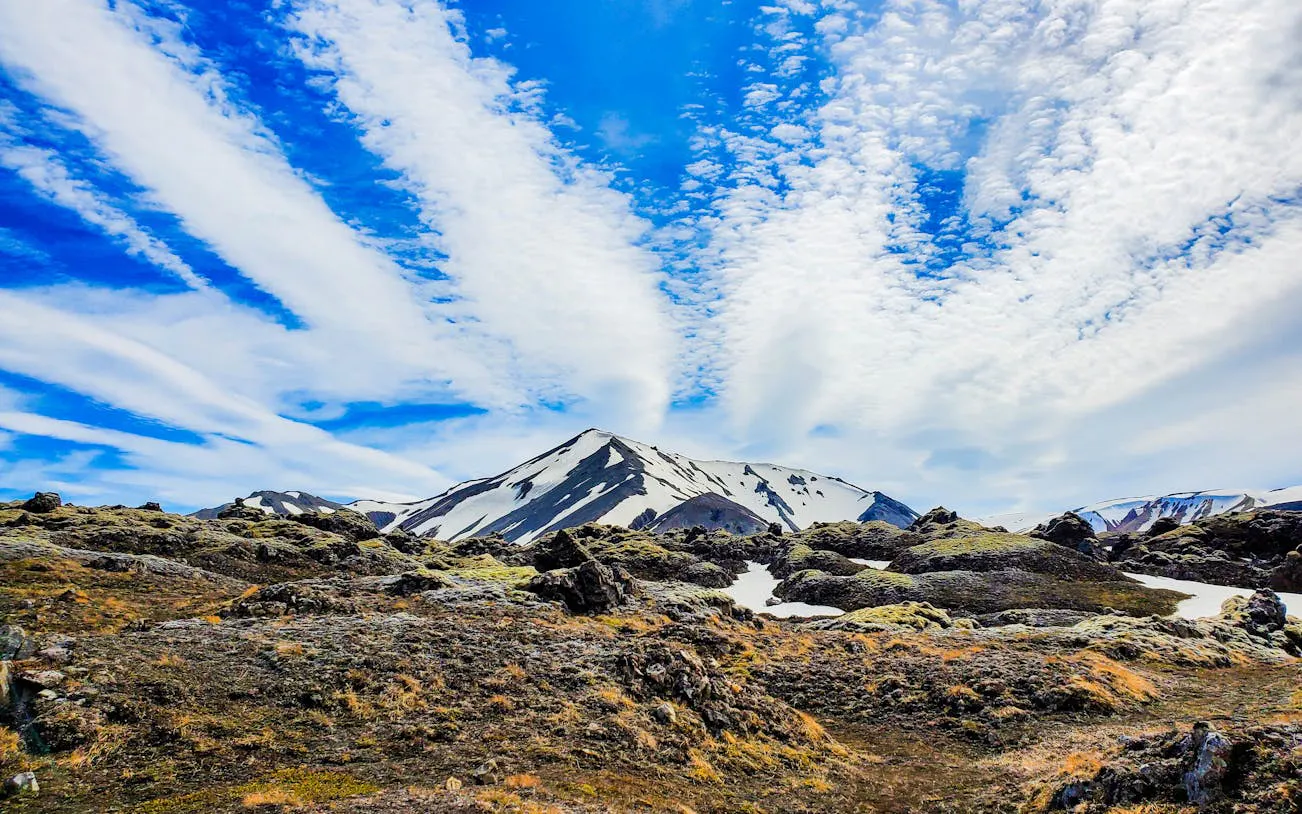 Landmannalaugar Highlands with snow-capped peaks and rocky terrain under a blue sky.