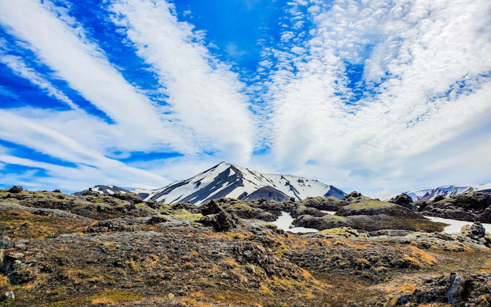 Landmannalaugar Highlands with snow-capped peaks and rocky terrain under a blue sky.