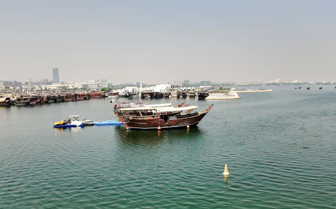Traditional dhow boat on the water with Doha cityscape in the background.