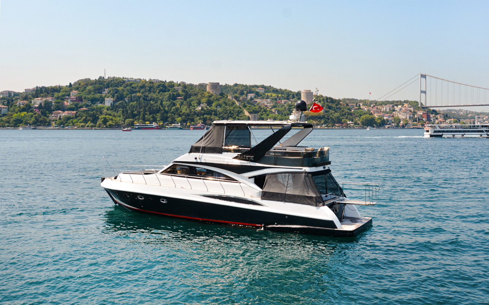 Luxury private yacht cruising on the Bosphorus with Istanbul skyline and bridge in the background.