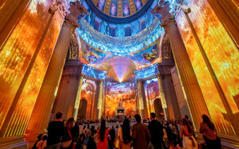 Immersive light show at Invalides, Paris, with vibrant projections on columns and dome.