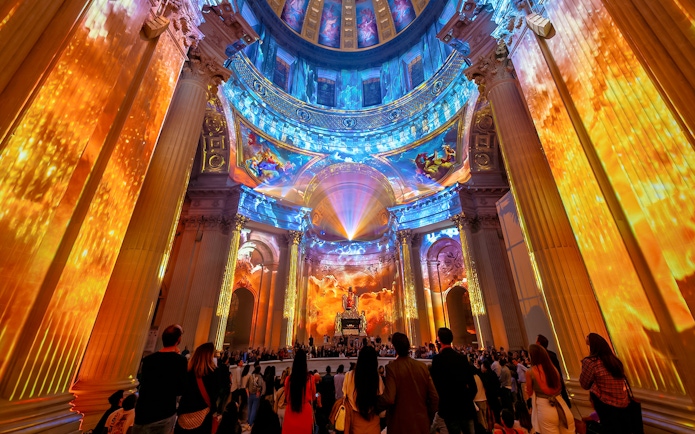 Immersive light show at Invalides, Paris, with vibrant projections on columns and dome.