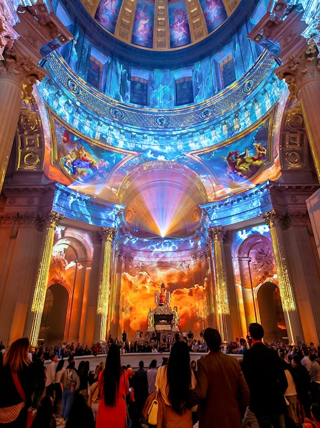 Immersive light show at Invalides, Paris, with vibrant projections on columns and dome.