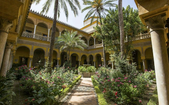 Courtyard garden with arches and palm trees in Seville Old Town.