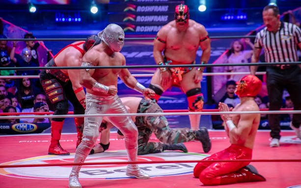 Wrestlers in colorful masks and costumes performing in a lucha libre match in Mexico.